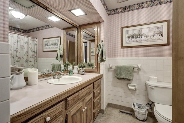 bathroom with tile patterned flooring, wainscoting, wallpapered walls, and toilet