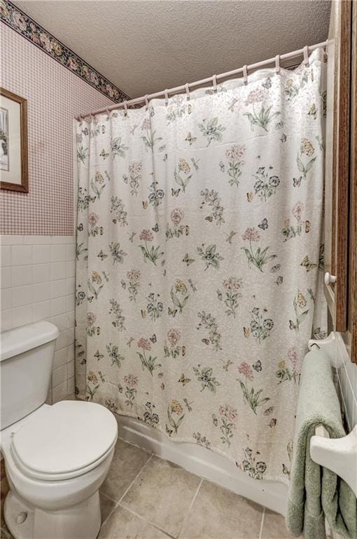 bathroom with tile patterned flooring, wainscoting, a textured ceiling, and wallpapered walls