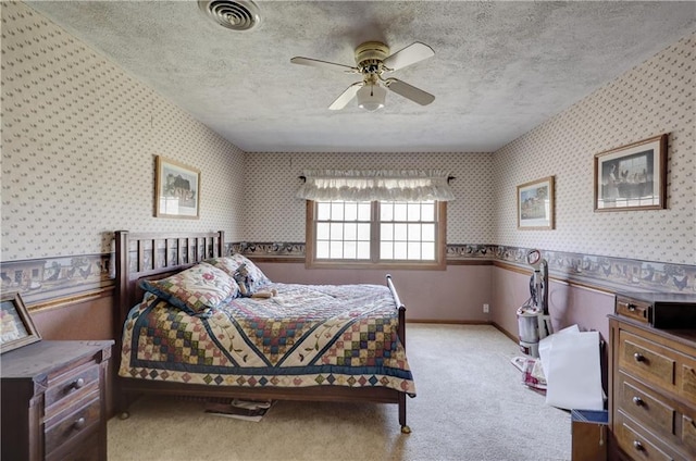 carpeted bedroom with wallpapered walls, a wainscoted wall, visible vents, and a textured ceiling