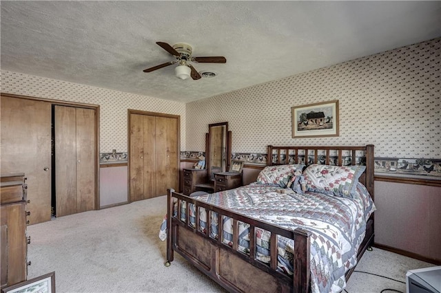 bedroom featuring a textured ceiling, wallpapered walls, multiple closets, and carpet floors