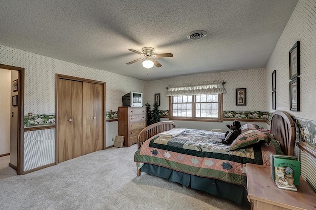 carpeted bedroom with a closet, visible vents, a textured ceiling, and wallpapered walls