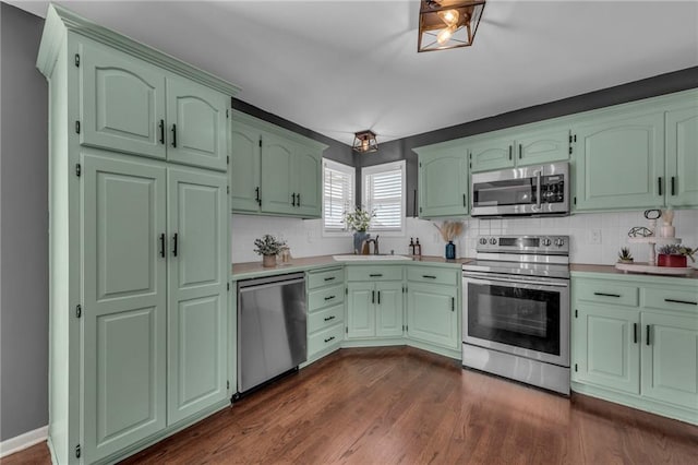 kitchen with green cabinetry, dark wood-style flooring, a sink, light countertops, and appliances with stainless steel finishes