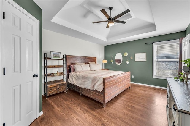 bedroom with a ceiling fan, a tray ceiling, dark wood-style floors, and baseboards