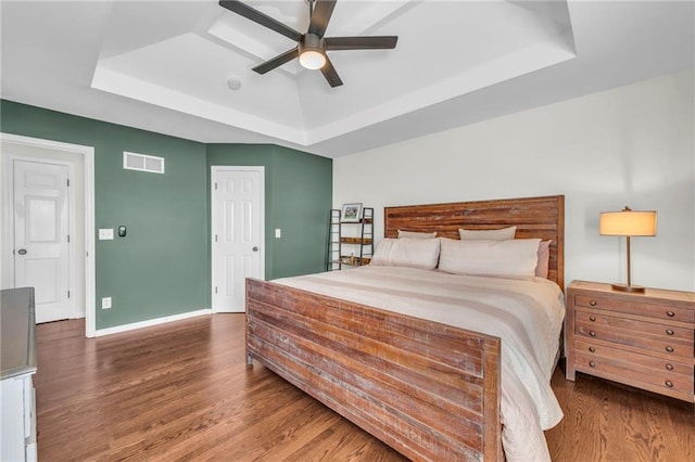 bedroom featuring visible vents, baseboards, a tray ceiling, wood finished floors, and a ceiling fan