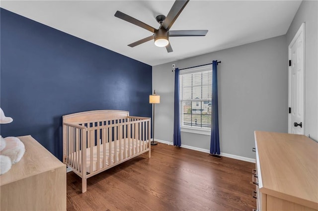 bedroom featuring baseboards, a nursery area, wood finished floors, and a ceiling fan