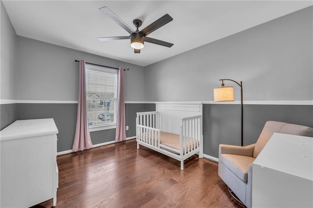 bedroom featuring baseboards, a nursery area, wood finished floors, and a ceiling fan