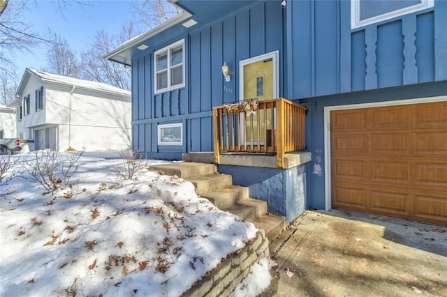 snow covered property entrance with a garage and board and batten siding