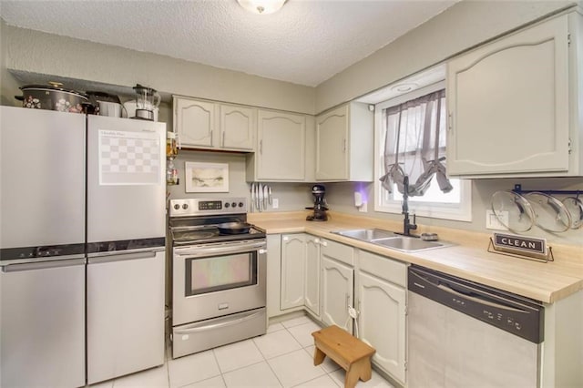 kitchen with a sink, a textured ceiling, appliances with stainless steel finishes, light countertops, and light tile patterned floors