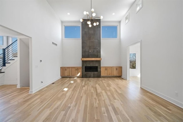 unfurnished living room with visible vents, a tile fireplace, stairs, light wood-type flooring, and a chandelier