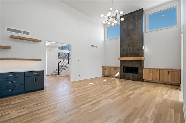 unfurnished living room with visible vents, an inviting chandelier, stairs, and light wood finished floors