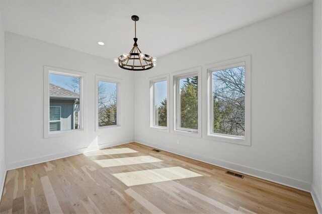 spare room featuring visible vents, baseboards, an inviting chandelier, and wood finished floors