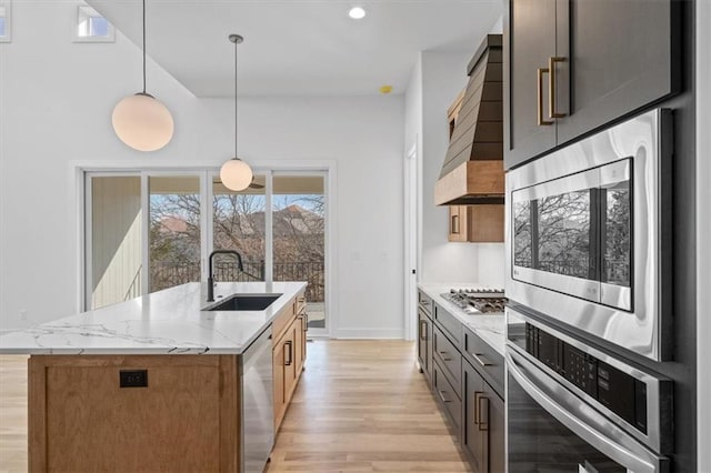 kitchen featuring light stone countertops, a sink, hanging light fixtures, stainless steel appliances, and light wood-style floors