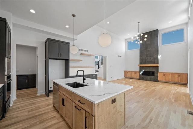 kitchen with visible vents, light stone countertops, light wood-type flooring, a high ceiling, and a sink