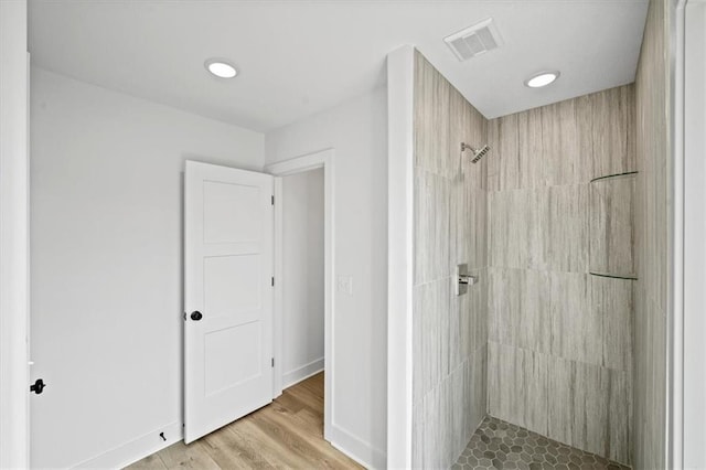 bathroom featuring visible vents, tiled shower, baseboards, and wood finished floors