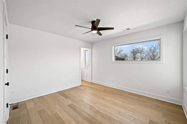 empty room featuring a ceiling fan, visible vents, light wood-style floors, and baseboards