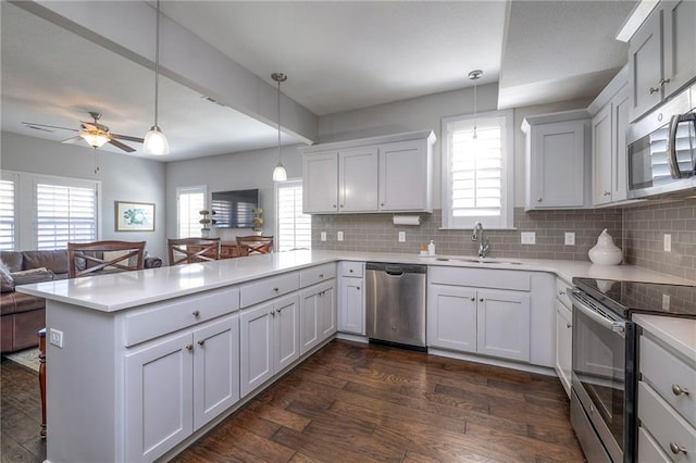 kitchen with a peninsula, dark wood-style flooring, light countertops, appliances with stainless steel finishes, and open floor plan