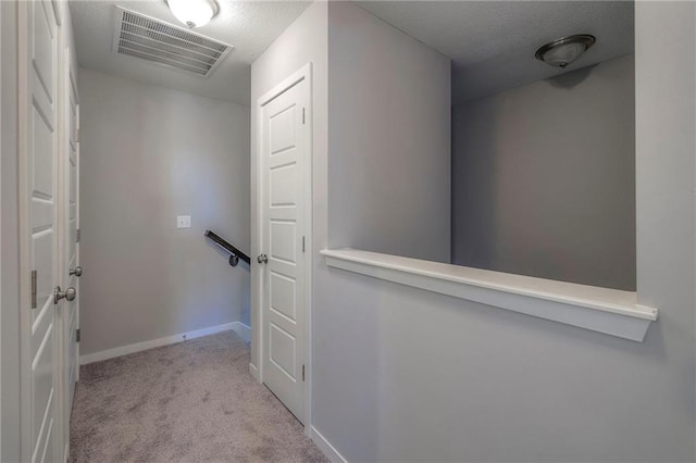 corridor featuring visible vents, baseboards, carpet, and a textured ceiling