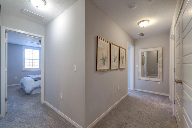 hallway featuring carpet flooring, baseboards, visible vents, and a textured ceiling