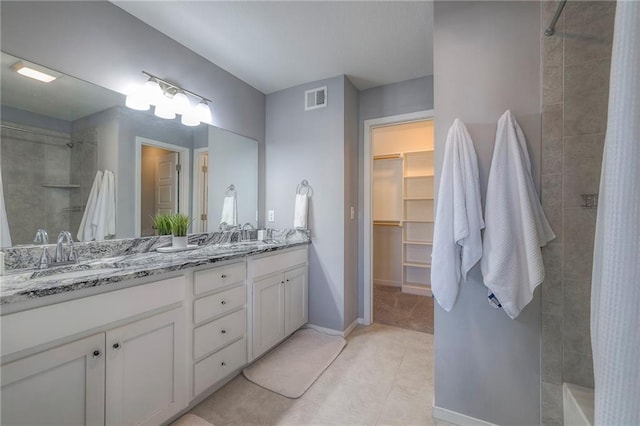 bathroom with visible vents, a walk in closet, a sink, double vanity, and tiled shower