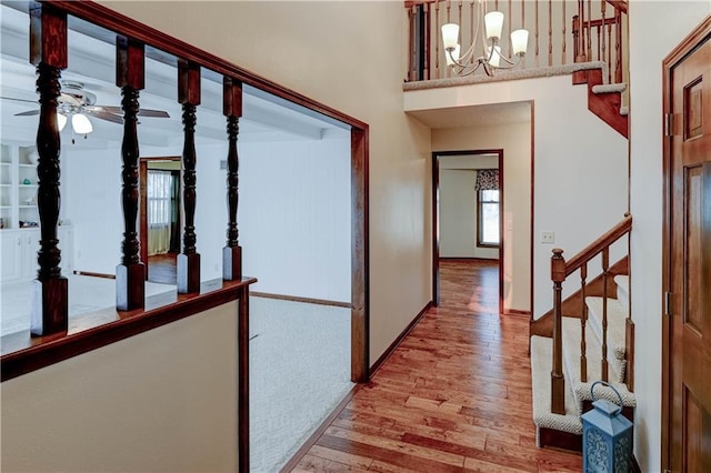 foyer entrance featuring baseboards, wood finished floors, stairs, and ceiling fan with notable chandelier