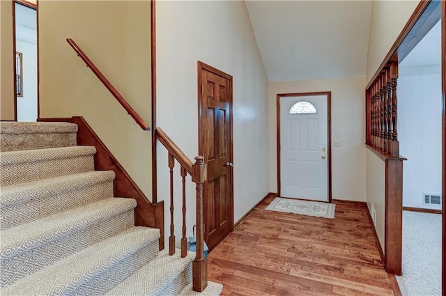 foyer entrance with wood finished floors, visible vents, baseboards, high vaulted ceiling, and stairs