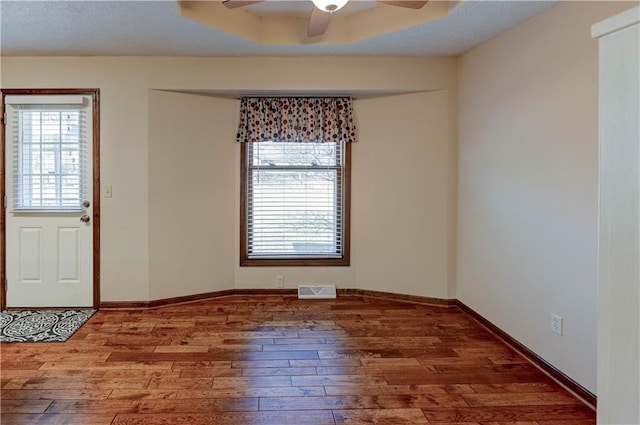 entrance foyer with visible vents, a raised ceiling, a ceiling fan, hardwood / wood-style flooring, and baseboards