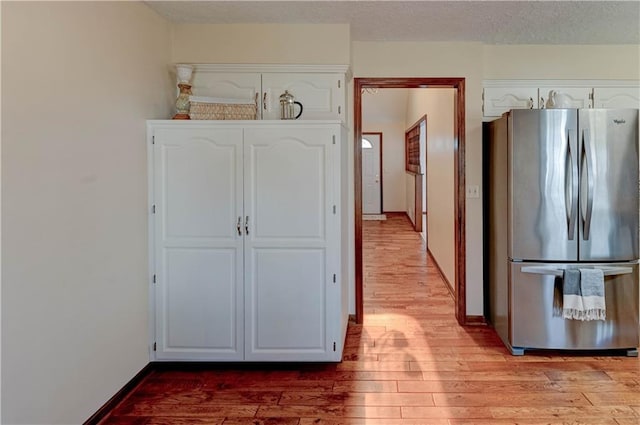 kitchen with white cabinetry, light wood-style floors, freestanding refrigerator, and a textured ceiling