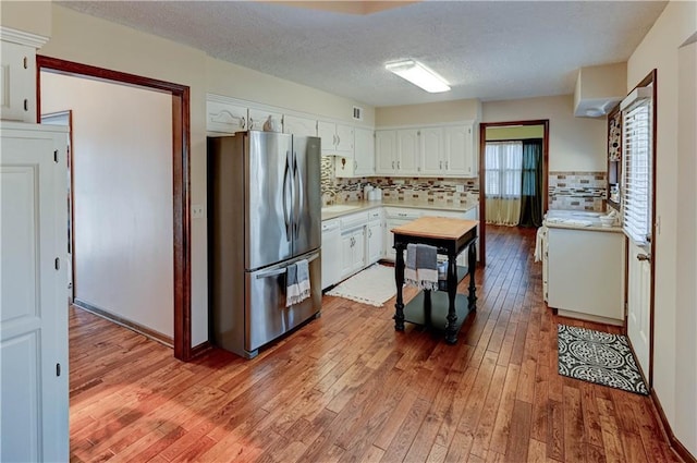 kitchen featuring hardwood / wood-style flooring, backsplash, freestanding refrigerator, white cabinets, and light countertops