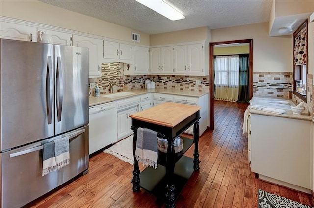 kitchen with visible vents, a sink, white cabinetry, freestanding refrigerator, and dishwasher