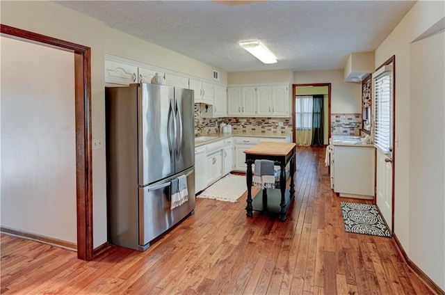 kitchen featuring light countertops, decorative backsplash, light wood-style flooring, freestanding refrigerator, and white cabinets