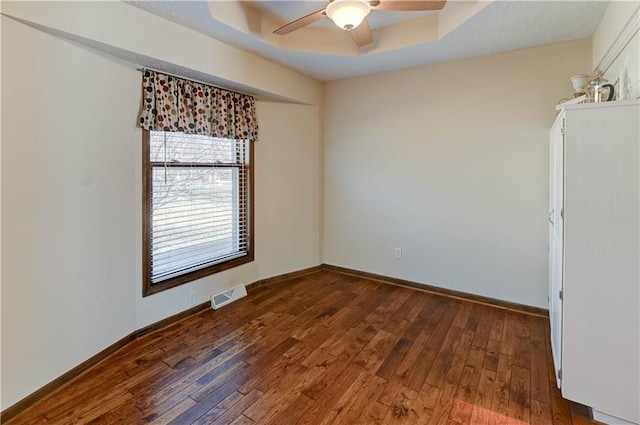 empty room featuring visible vents, baseboards, a raised ceiling, ceiling fan, and dark wood-style flooring