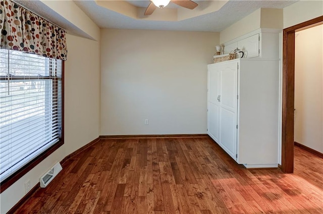 unfurnished bedroom featuring visible vents, ceiling fan, baseboards, a raised ceiling, and wood-type flooring