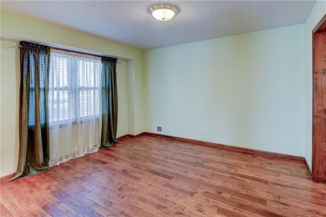 spare room featuring hardwood / wood-style flooring, baseboards, visible vents, and a textured ceiling