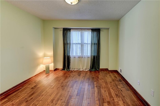 unfurnished room with a textured ceiling, baseboards, and hardwood / wood-style flooring