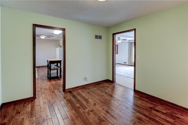 empty room featuring visible vents, baseboards, a textured ceiling, and dark wood-style floors