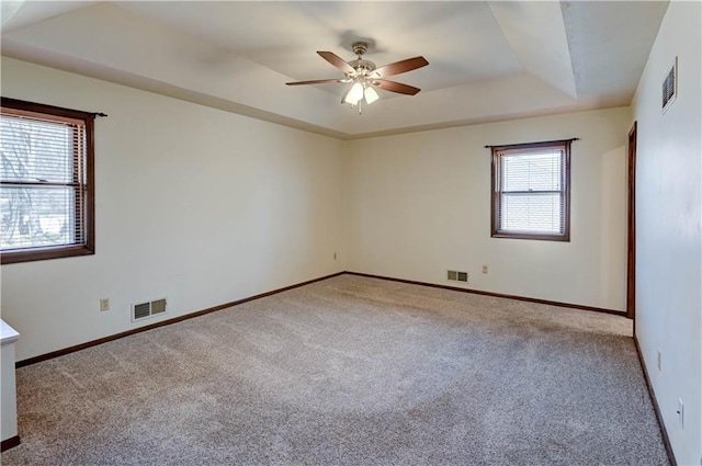 carpeted empty room with visible vents, a raised ceiling, baseboards, and a ceiling fan