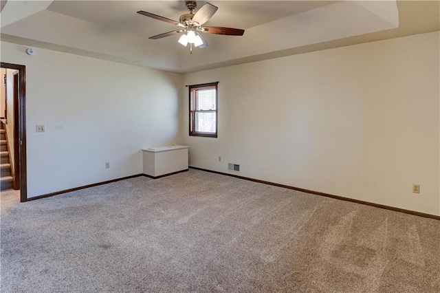 empty room featuring light carpet, visible vents, a raised ceiling, and a ceiling fan