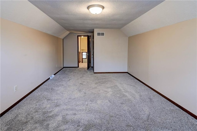 additional living space featuring visible vents, a textured ceiling, baseboards, and vaulted ceiling