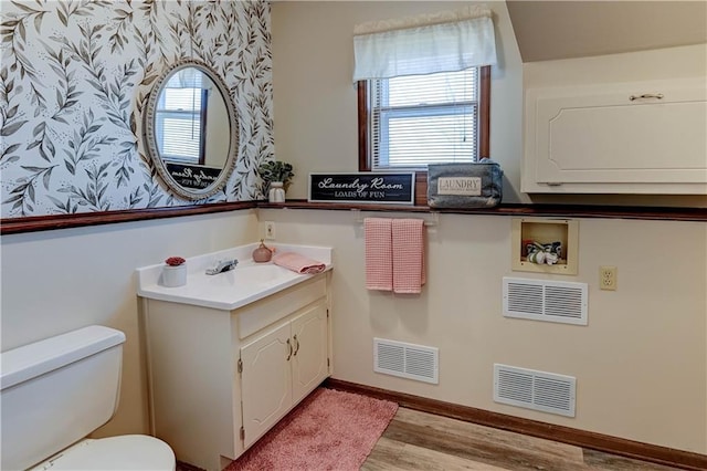 half bathroom featuring vanity, toilet, wood finished floors, and visible vents