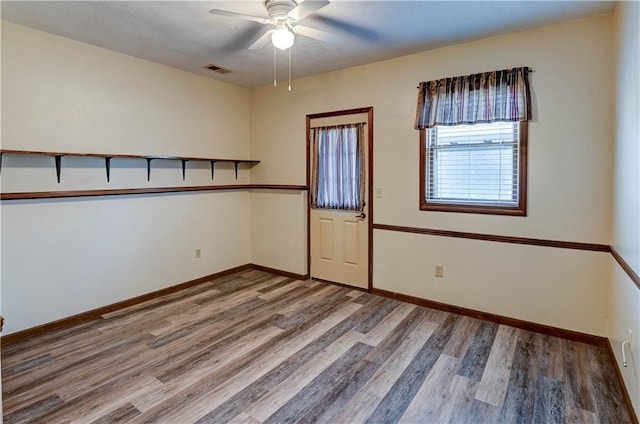 unfurnished room with ceiling fan, visible vents, baseboards, and wood finished floors