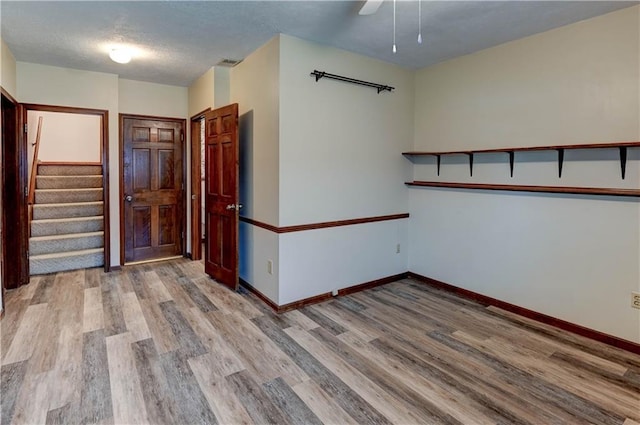 empty room with stairway, baseboards, a textured ceiling, and wood finished floors