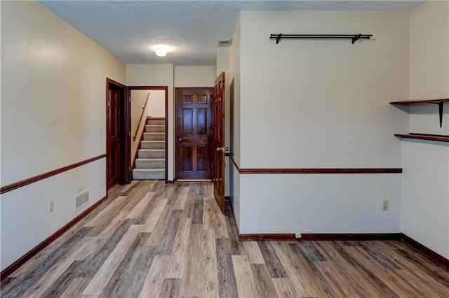 empty room with visible vents, a textured ceiling, wood finished floors, stairway, and baseboards