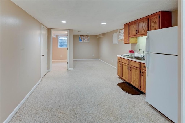 kitchen featuring baseboards, light countertops, brown cabinets, freestanding refrigerator, and a sink