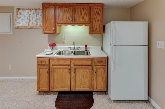 kitchen featuring light countertops, baseboards, freestanding refrigerator, and a sink