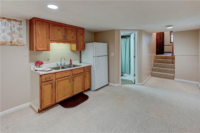 kitchen featuring baseboards, light countertops, light carpet, freestanding refrigerator, and a sink