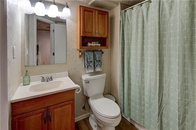 bathroom featuring toilet, curtained shower, wood finished floors, vanity, and a textured wall