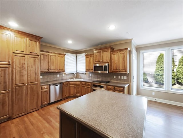 kitchen featuring light wood finished floors, a sink, stainless steel appliances, crown molding, and backsplash