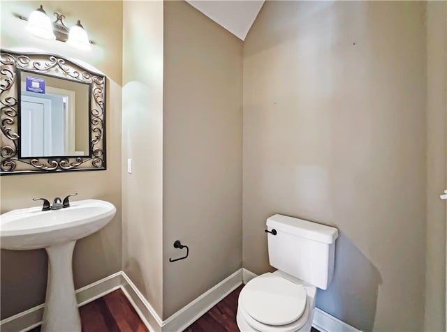 half bathroom with a sink, toilet, baseboards, and wood finished floors