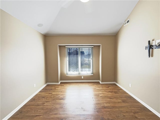 unfurnished room featuring vaulted ceiling, baseboards, visible vents, and wood finished floors