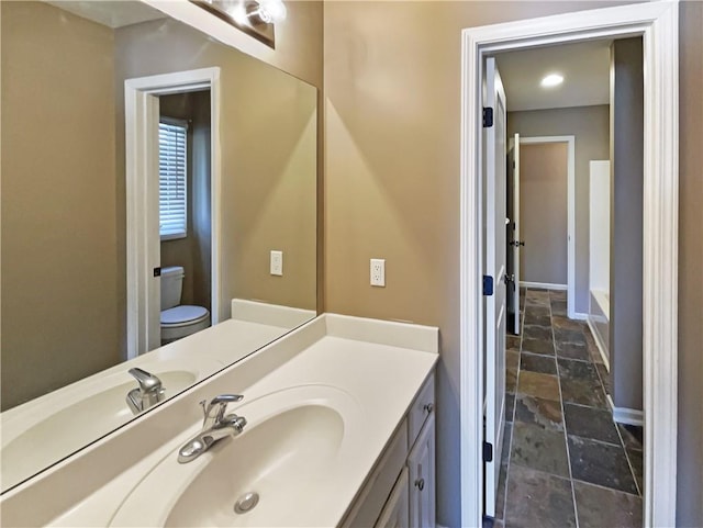 bathroom featuring baseboards, toilet, vanity, and stone finish floor